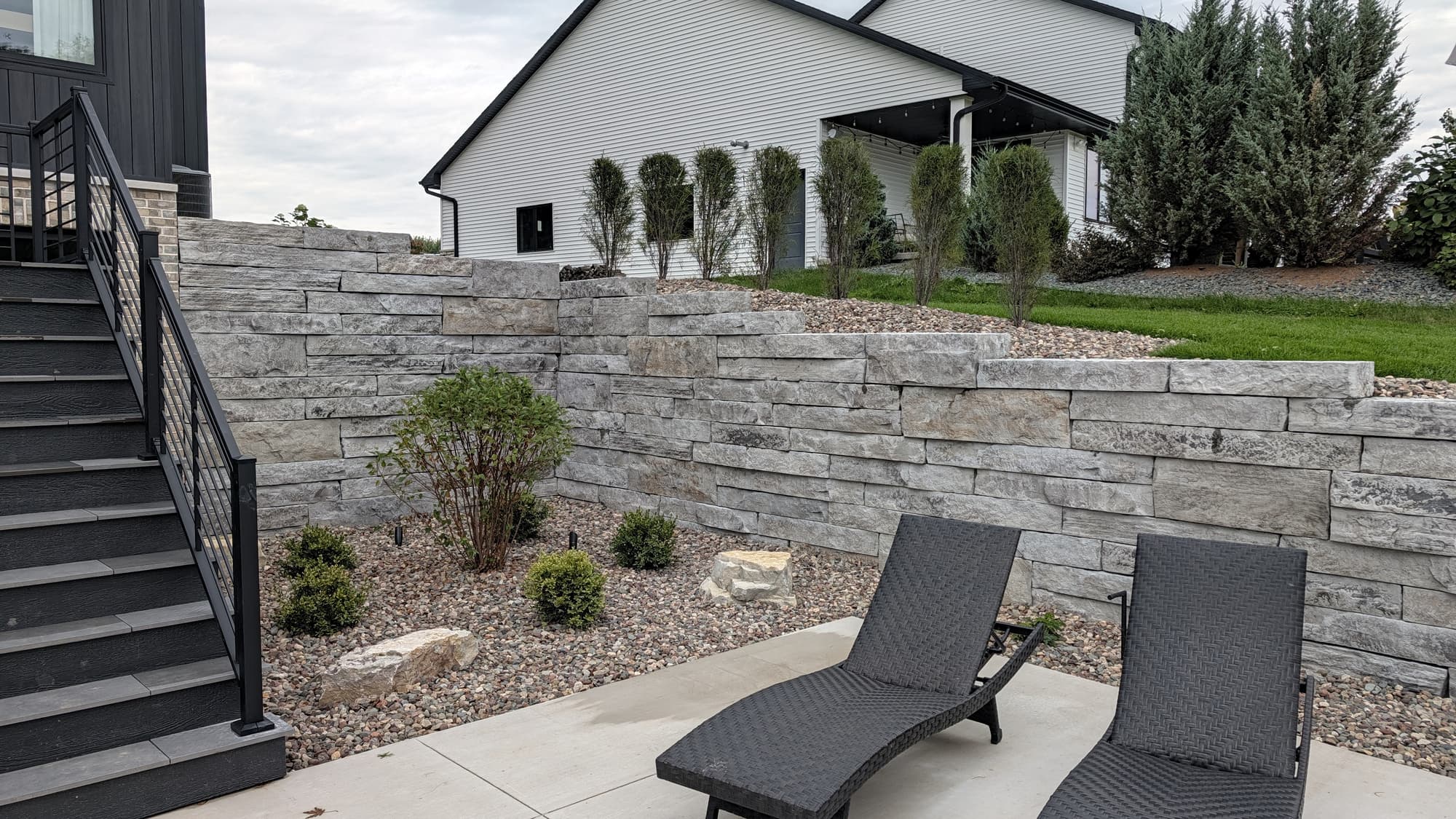 Stepped retaining wall built with stone-textured concrete blocks beside a patio and planting beds.